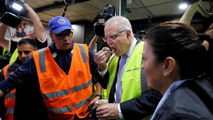 Scott Morrison eats a chestnut in the markets while Jenny Morrison watches on