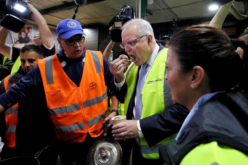 Scott Morrison eats a chestnut in the markets while Jenny Morrison watches on