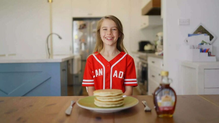 Child standing behind a table with pancakes and a maple syrup bottle on it