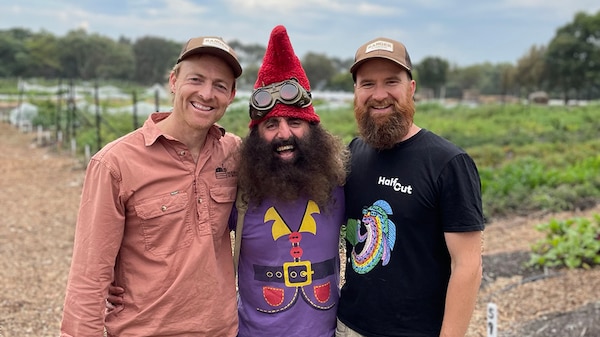 Costa the Garden Gnome standing with two men in a school garden.