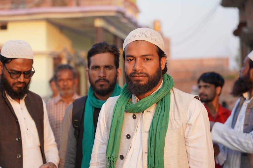 Man wearing white with a green scarf with other supporters behind him.