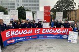 Nurses in their uniforms stand behind a large banner reading "enough is enough"