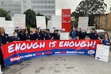 Nurses in their uniforms stand behind a large banner reading "enough is enough"