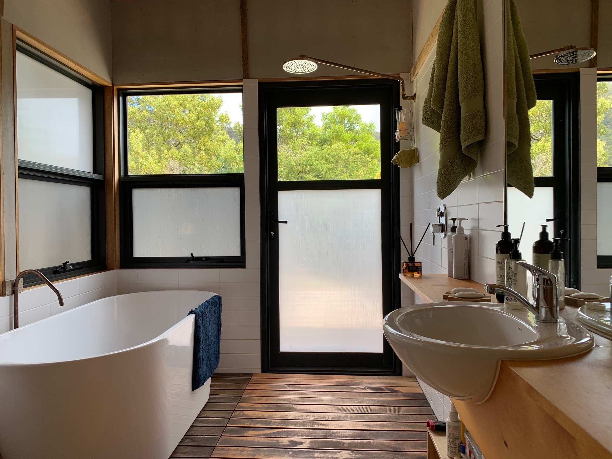 A bathroom, showing a vanity, standalone bathtub and a shower. The window looks out to treetops