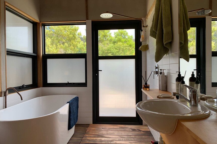 A bathroom, showing a vanity, standalone bathtub and a shower. The window looks out to treetops