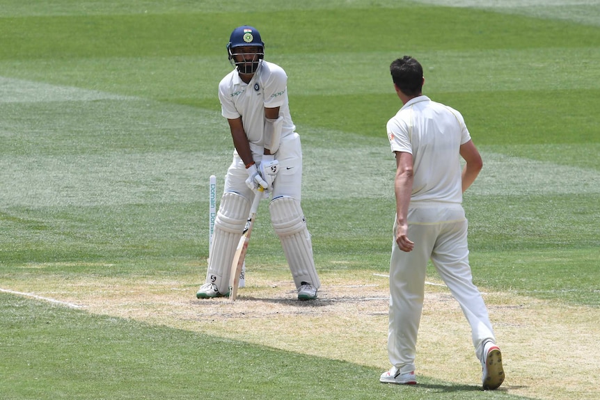 India batsman Cheteshwar Pujara stands in front of his stumps, with the bails removed, looking at Australia bowler Pat Cummins.