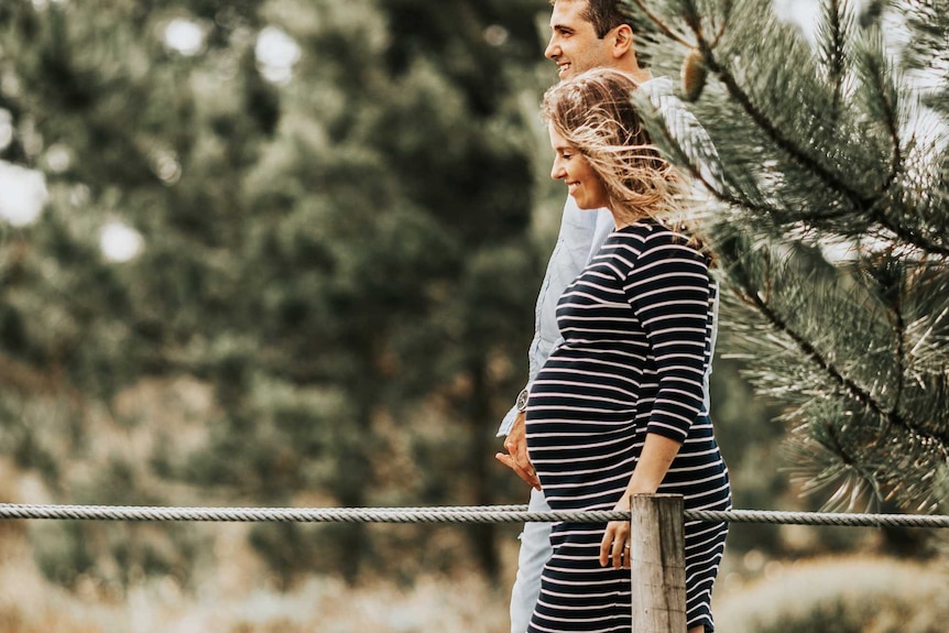 A man and a pregnant woman walk on a wooden walkway.