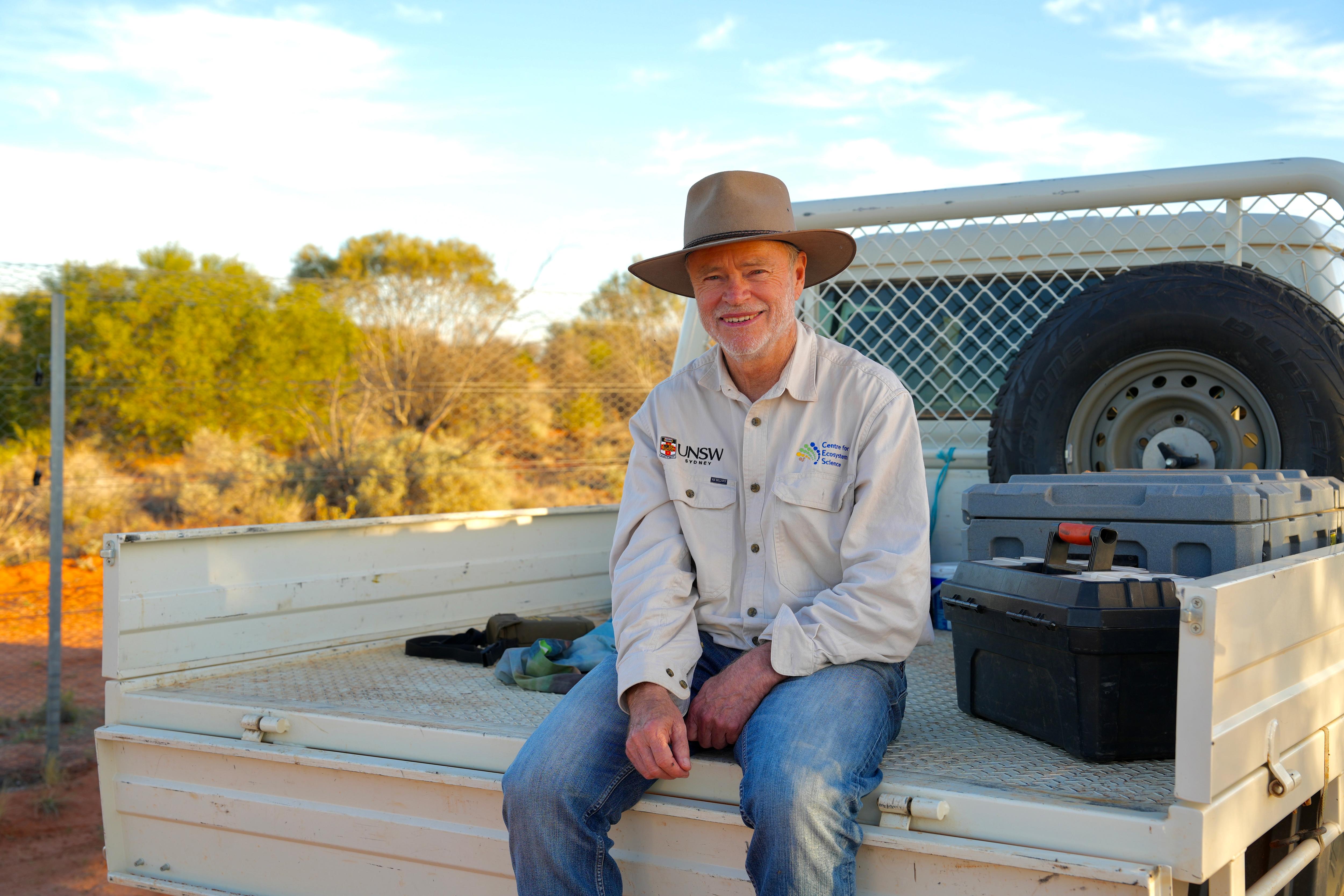 Hombre sentado en la parte trasera de una ute blanca con jeans, camisa ligera y sombrero.