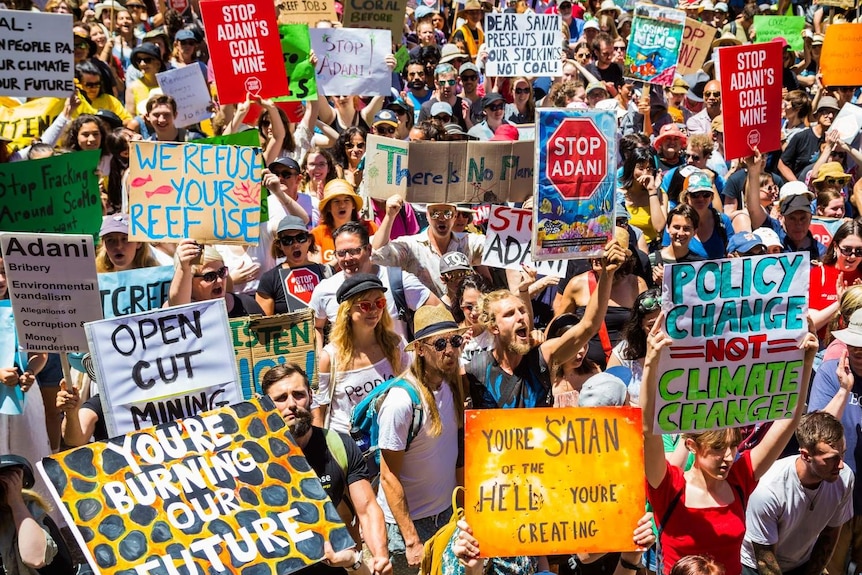 Crowds holding anti-Adani and climate change signs and chanting.