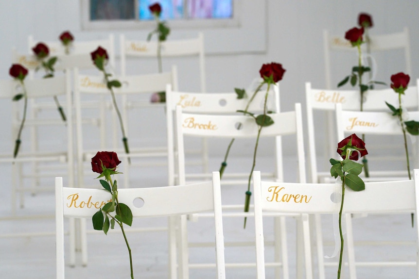Red roses rest against white chairs with names written on them in gold.