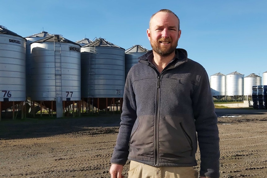 A man stands in front of a row of large grain silos