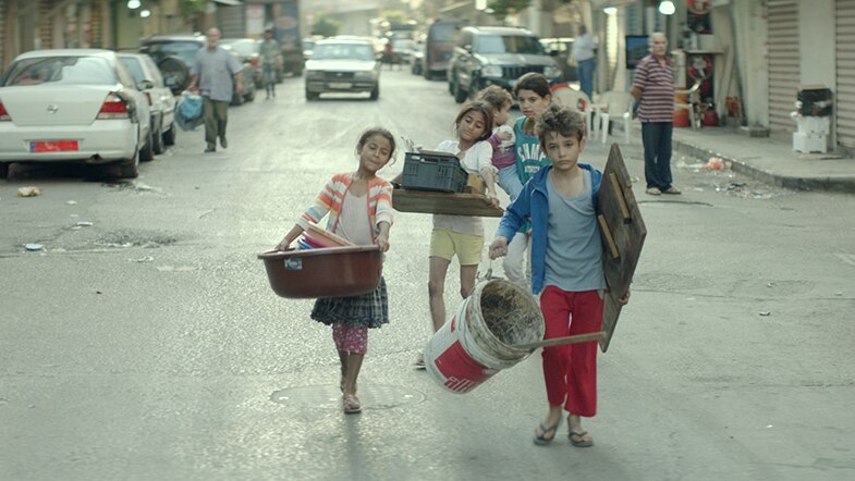 Colour still of Zain Al Rafeea and other children in the street carrying items in 2018 film Capharnaüm.