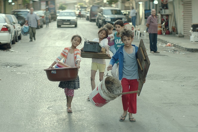 Colour still of Zain Al Rafeea and other children in the street carrying items in 2018 film Capharnaüm.