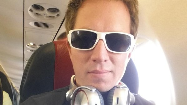 Jonathan William Parker wearing white sunglasses takes a selfie while sitting on a plane.