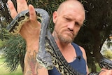 Bryan holds up the snake's head, which is curled around his arms
