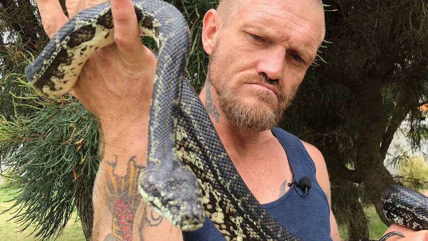 Bryan holds up the snake's head, which is curled around his arms
