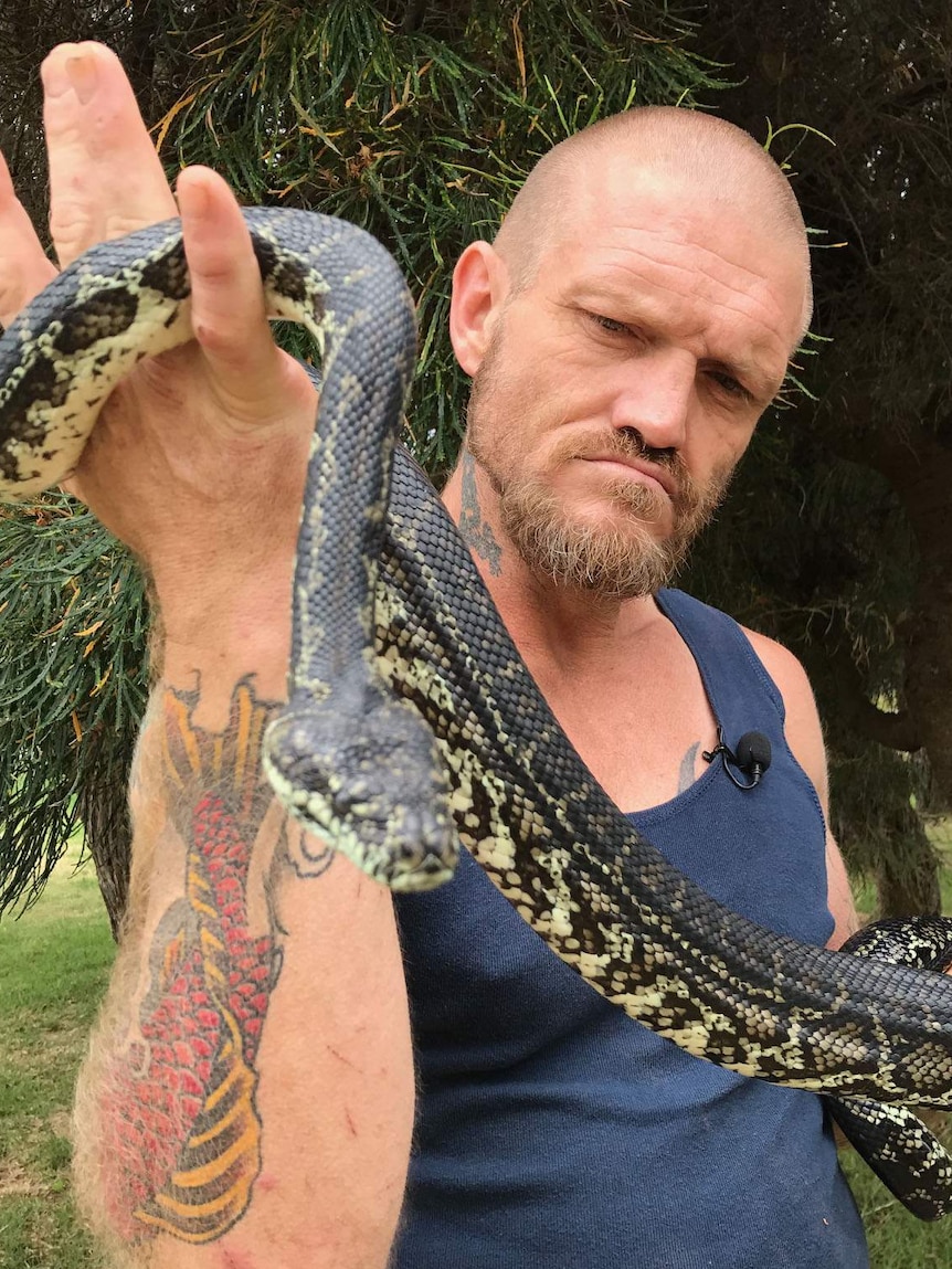 Bryan holds up the snake's head, which is curled around his arms