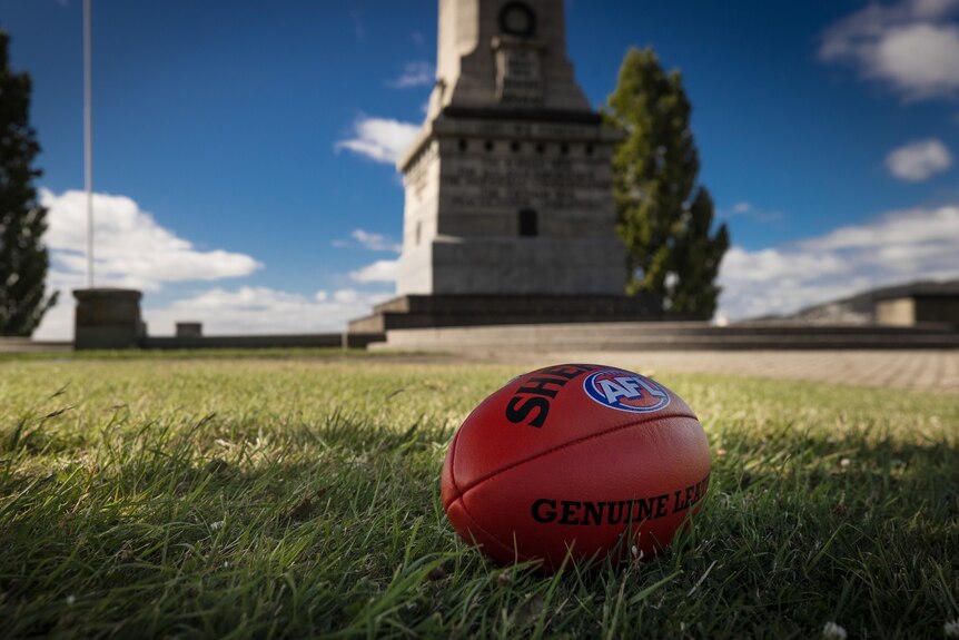Красный футбольный мяч стоит на траве рядом с кенотафом Хобарта.