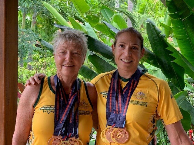 Two women stand in gold jerseys with several gold and bronze medals around their necks.