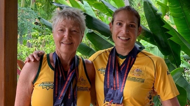 Two women stand in gold jerseys with several gold and bronze medals around their necks.
