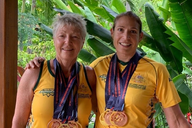 Two women stand in gold jerseys with several gold and bronze medals around their necks.