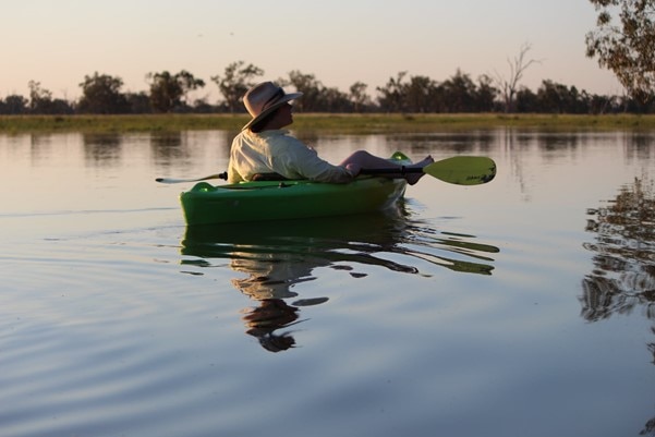 A man wearing an Akubra kayaking down a waterway.