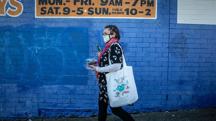 Elena Bermeister walks with a cake and drink bottle in front of a supermarket.