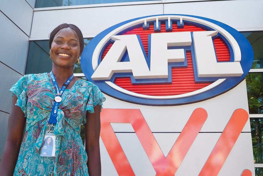 A smiling woman looking at the camera in front of a large blue, red and white AFL logo.