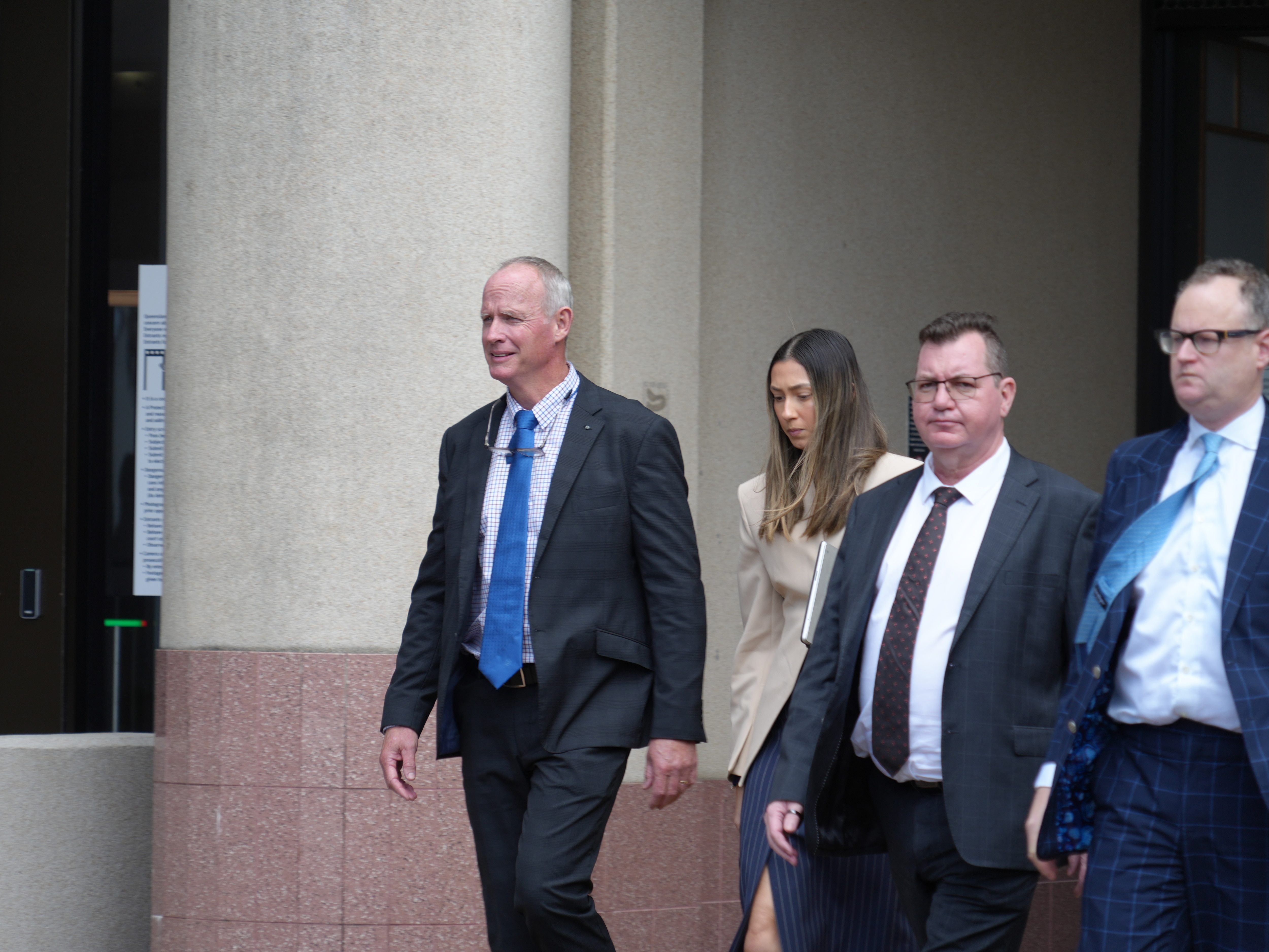 a man in blue tie and suit walks out of a courthouse with several other lawyers