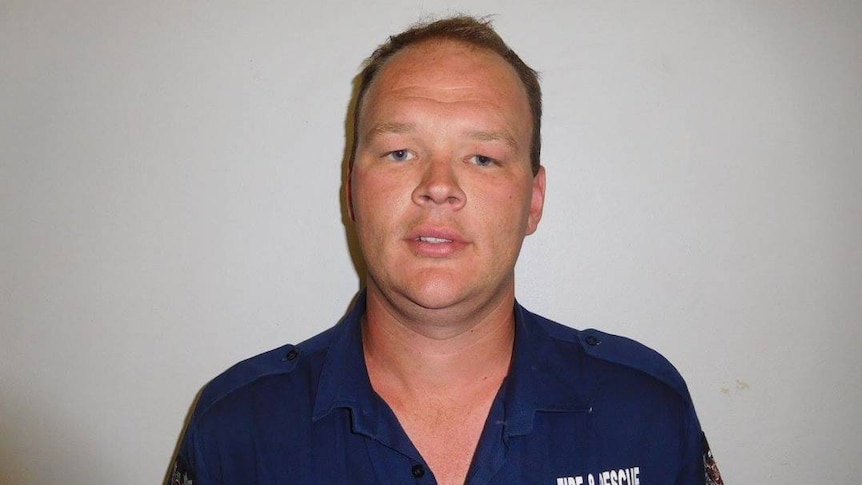A mugshot-style photograph of a balding man in his thirties, dressed in a fire-and-rescue shirt.