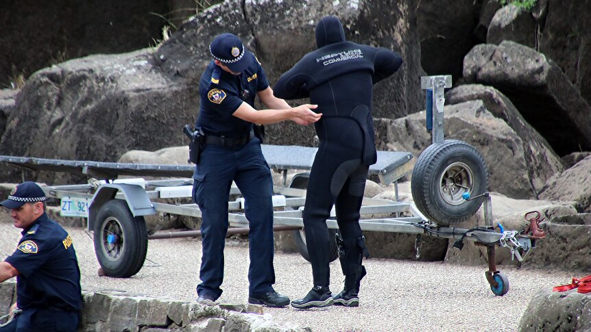 A police officer helps a diver pull on their wetsuit and gear.
