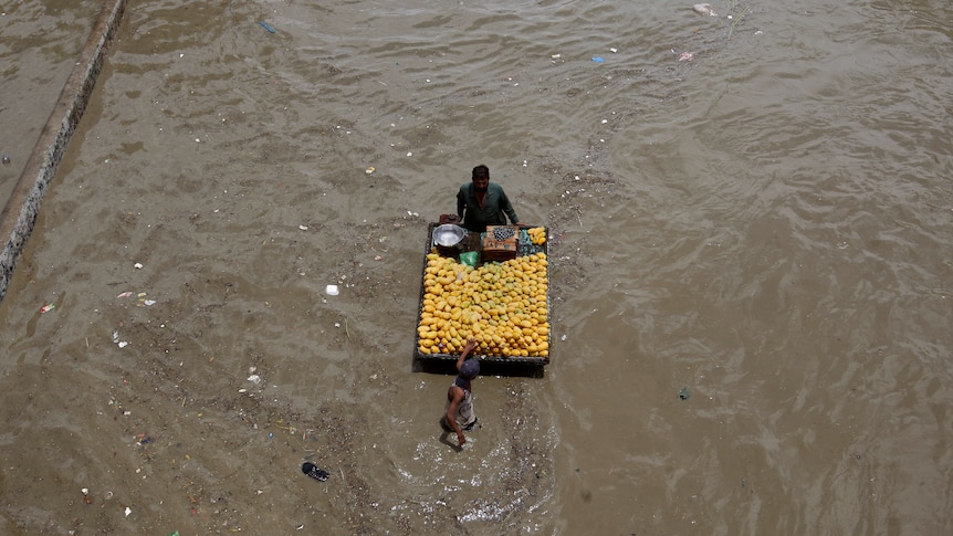 A fruit seller wheels a cart of yellow fruit through a flooded road after a heavy rainfall in Karachi.