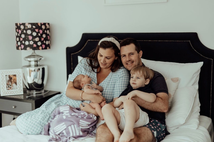 Anthea Marsh, her husband, young son and newborn sit on a bed.