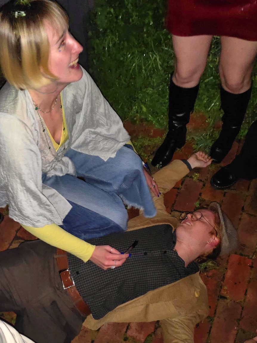 Oliver Lees lies on the ground pretending to be dead while a friend kneels beside him.