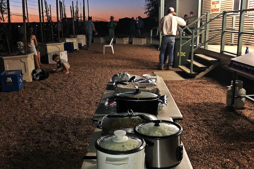 Pots of hot food sits on a table in a makeshift outdoor kitchen