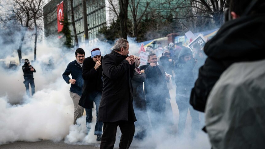 Men run and cover their faces as Turkish anti-riot police officers use tear gas to disperse supporters in front of the headquarters of the Turkish daily newspaper Zaman