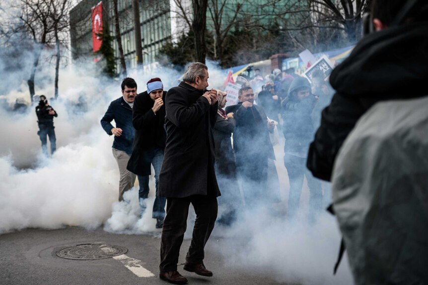 Men run and cover their faces as Turkish anti-riot police officers use tear gas to disperse supporters in front of the headquarters of the Turkish daily newspaper Zaman