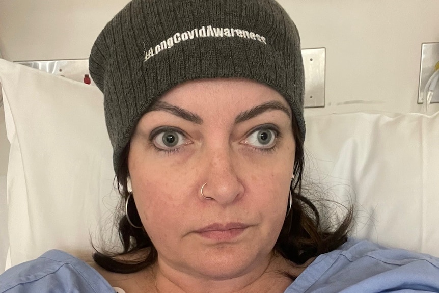 Woman in hospital bed wearing a "long COVID awareness" beanie.