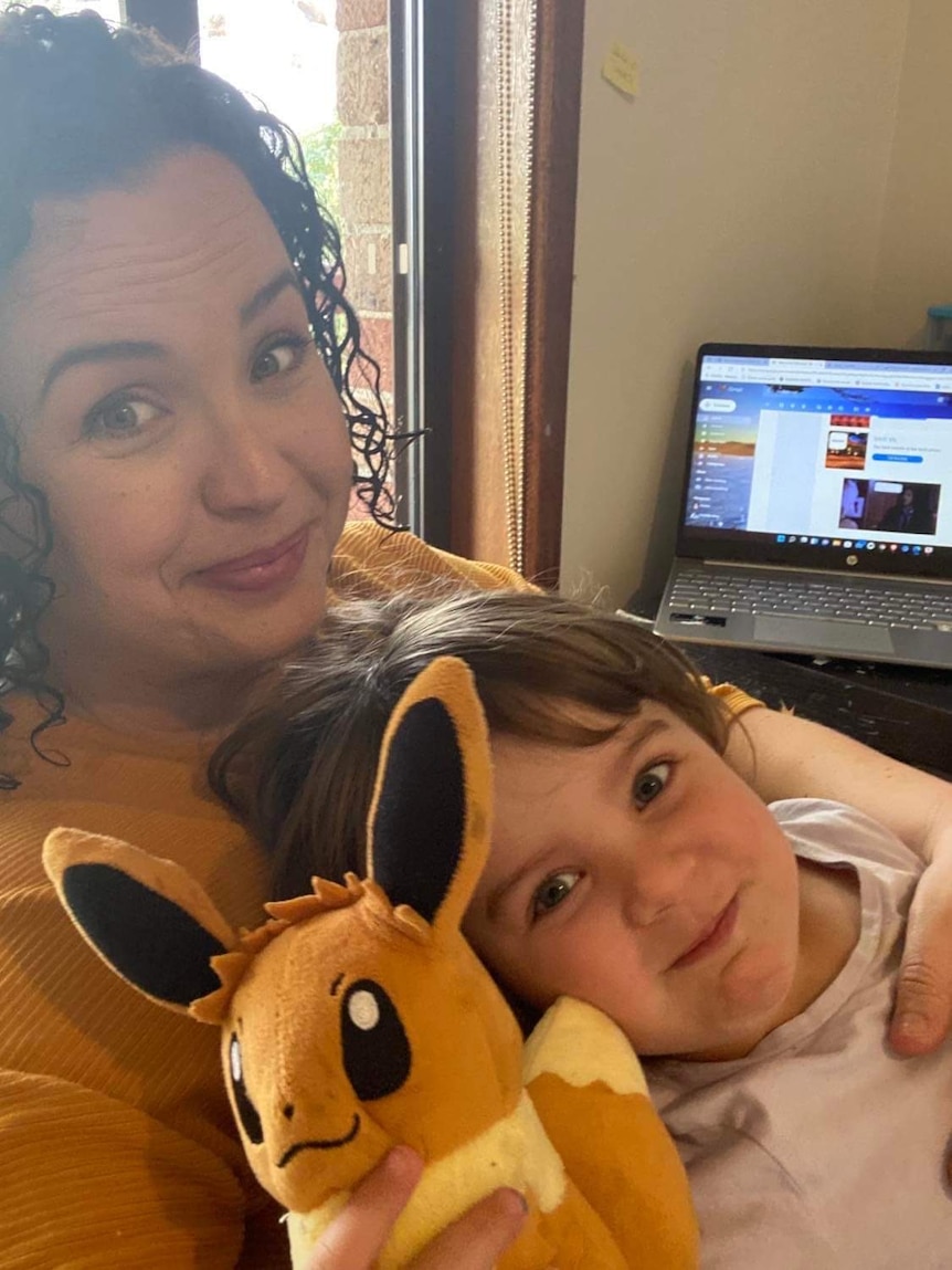 A girl sits on a woman's lap, holding a Pokemon stuffed toy