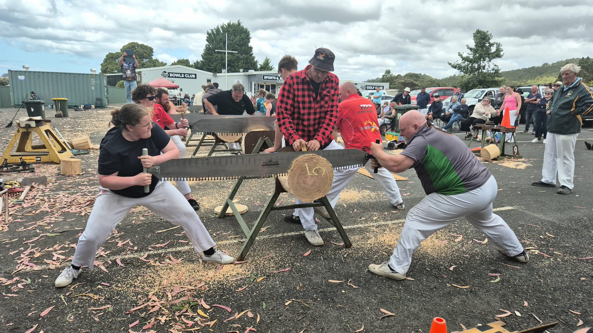 uma adolescente e seu pai estão em cada extremidade de uma longa lâmina de serra, serrando um tronco de madeira