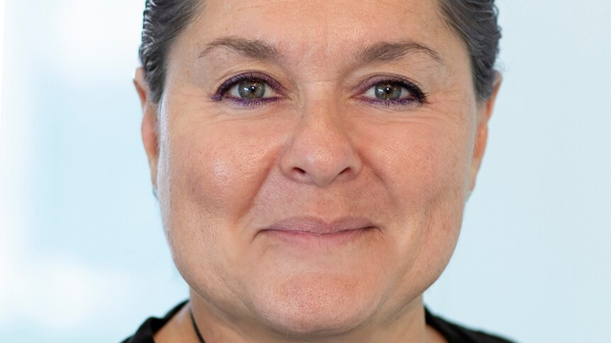 A professional head shot of a woman with slick back hair and dark eye makeup. 