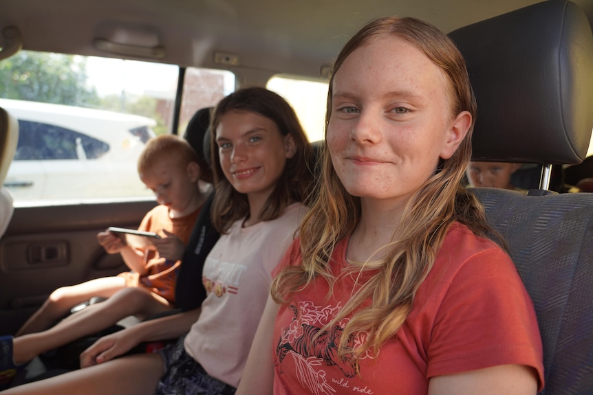 three kids sit in the back seat of a car