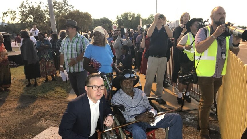 Alan Joyce squats as he talks to a member of the Kngwarreye family who sits in a wheelchair next to the media pack.