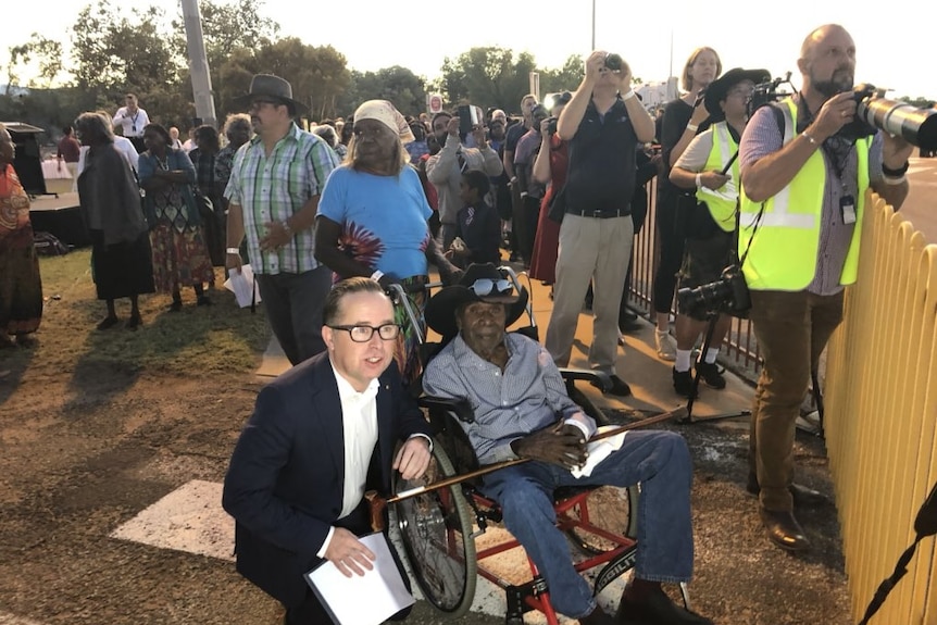 Alan Joyce squats as he talks to a member of the Kngwarreye family who sits in a wheelchair next to the media pack.