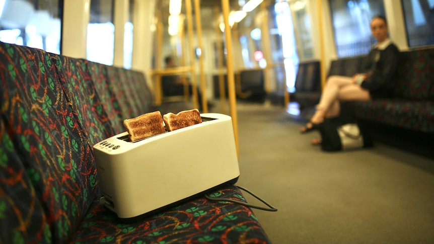 A toaster with two slices of toast popping out sits on a bench seat on a Perth train.