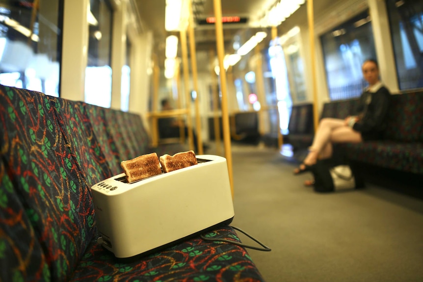 A toaster with two slices of toast popping out sits on a bench seat on a Perth train.