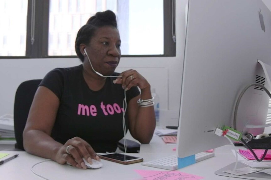 Tarana Burke sits at her computer with earphones on.