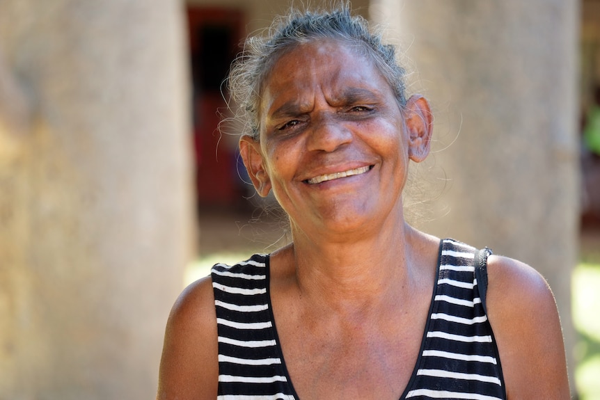 An Aboriginal woman in a horizontal-striped top looks to the camera and smiles.