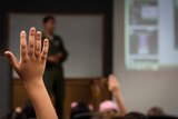 A student has their hand raised in a lecture.