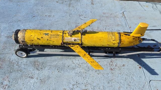 The yellow ocean glider on the deck of a boat, covered in barnacles.